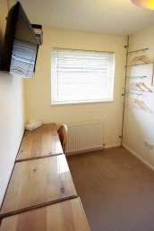 View of single bedroom's tabletop, TV, and chair